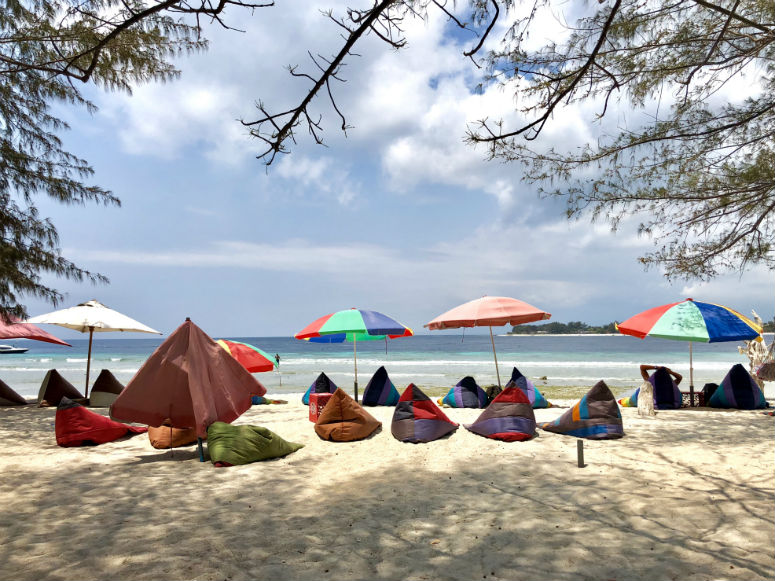 Strand mit bunten Schirmen und Sitzsäcken auf Gili Trawangan
