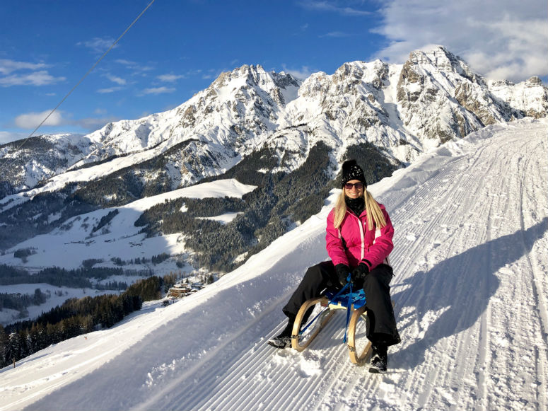 Frau auf Schlitten vor Bergpanorama