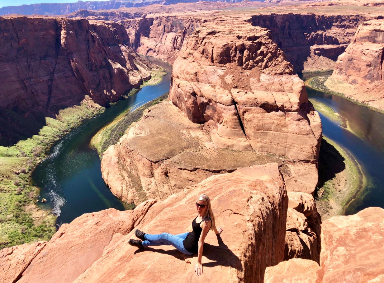 Nationalparks der USA, Frau sitzt vor Horseshoe Bend auf Felsen