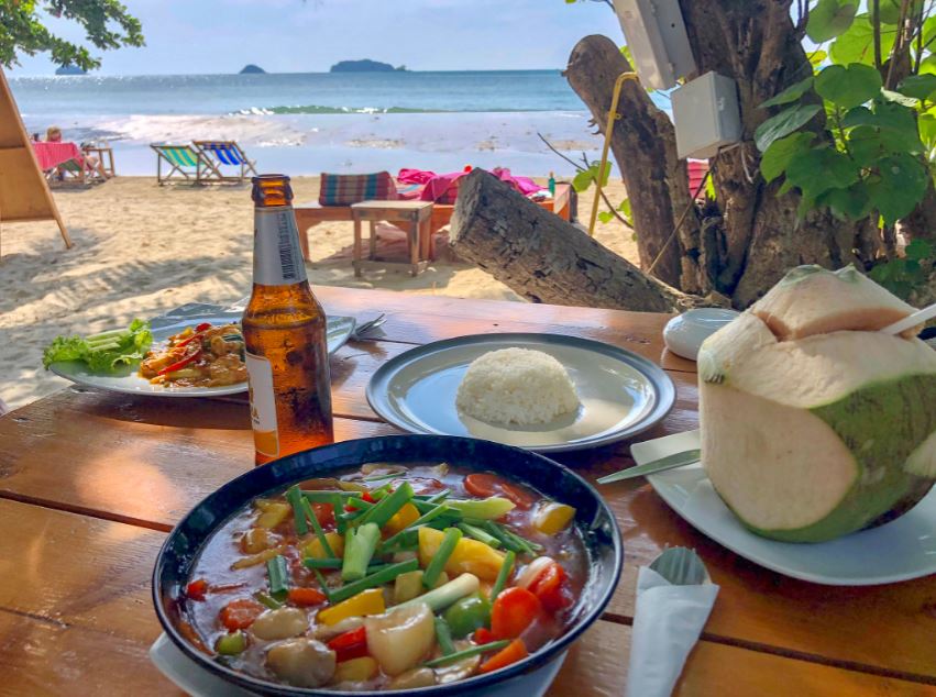 Thai-Curry, Reis, Kokosnuss und Bier auf Tisch mit Meerblick