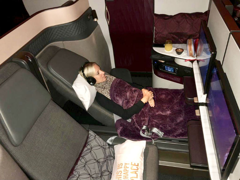 Amex Gold Card, Frau mit Kopfhörer sitzt in großem Abteil der Qatar Airways Business Class