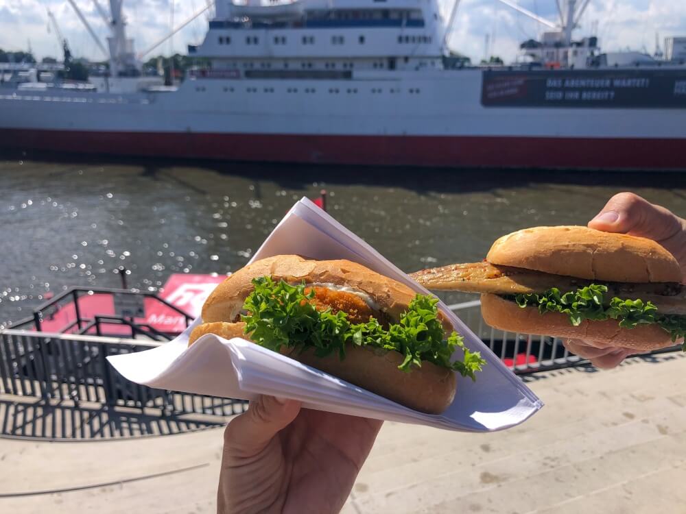 Zwei Fischsemmeln in der Hand mit Blick auf Schiff im Hamburger Hafen