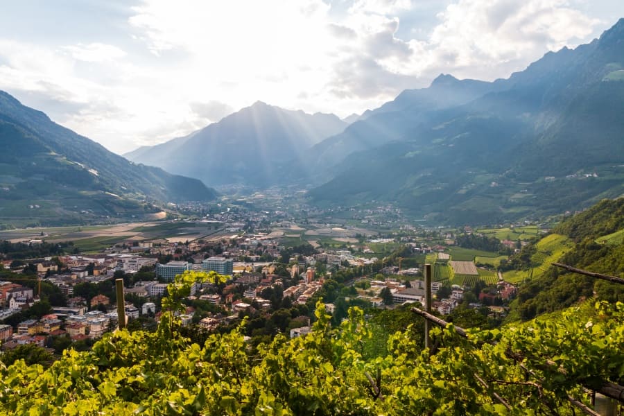 Unternehmungen rund um das Hotel Botango, Blick von oben auf Meran mit Sonnenstrahlen hinter Berg