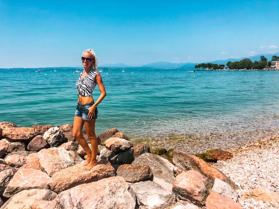 Frau steht auf Felsen am Kiesstrand am Gardasee