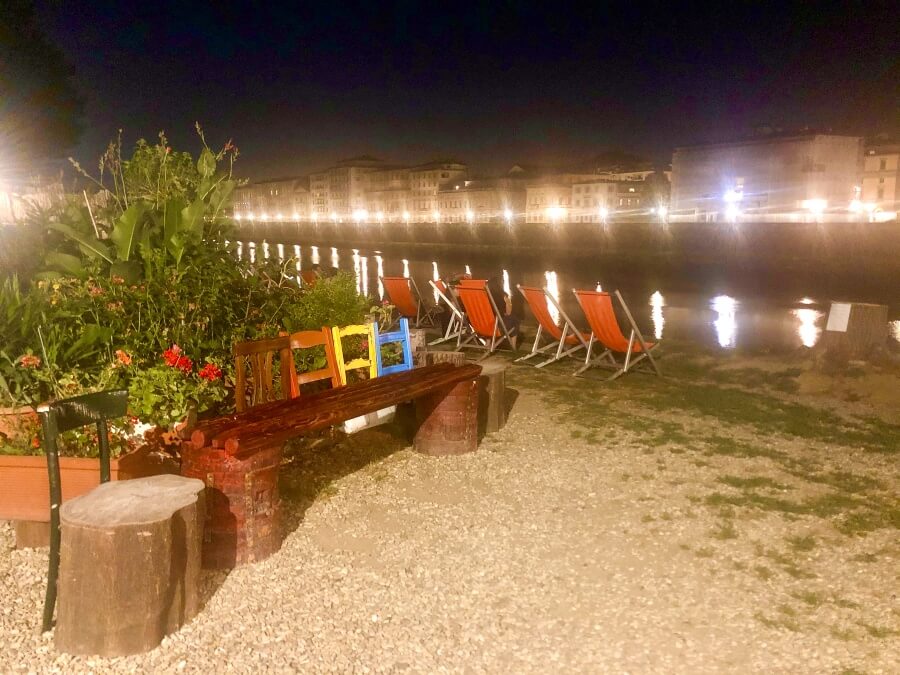 Biergarten mit bunten Stühlen direkt am Fluss Arno in Florenz