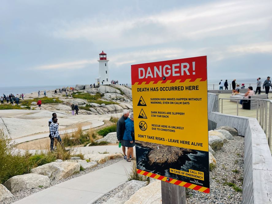 Schild an den Felsen von Peggys Cove mit der Warnung vor mitreißenden Wellen an den unteren Felsen