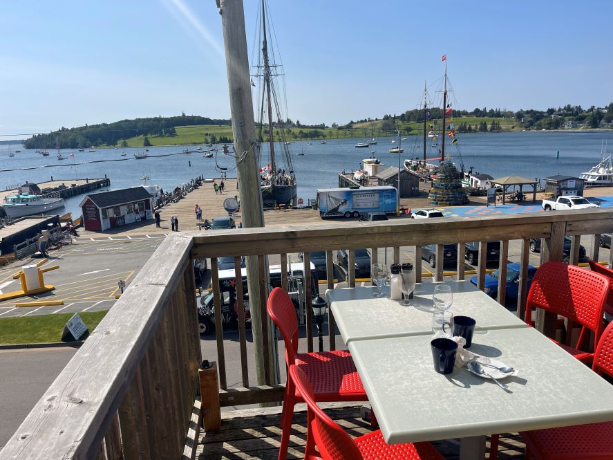 Tisch mit roten Stühlen auf Terrasse vor Restaurant Savvy Sailor in Lunenburg mit Blick auf Hafen