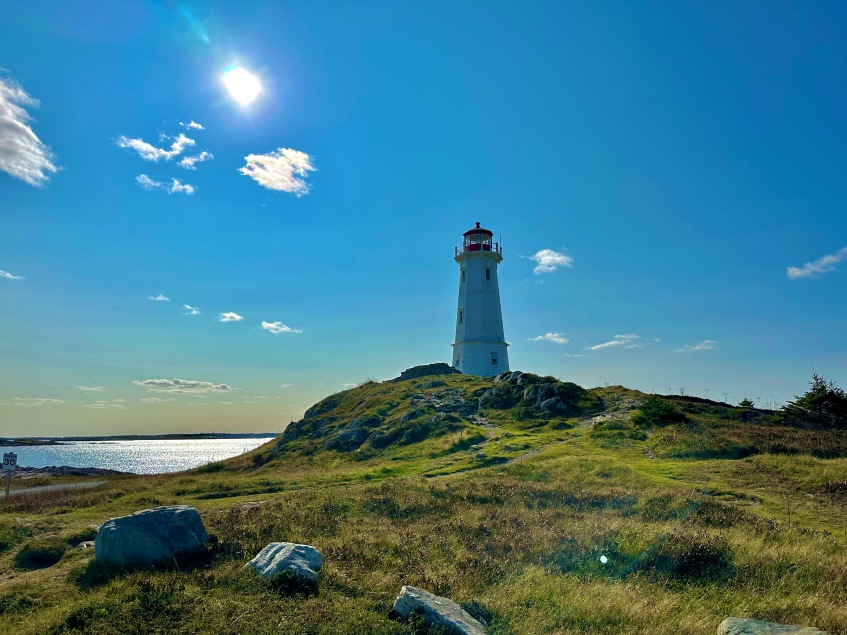 Der Leuchtturm von Louisbourg auf einem kleinen Hügel aus Gras und Felsen, blauer Himmel