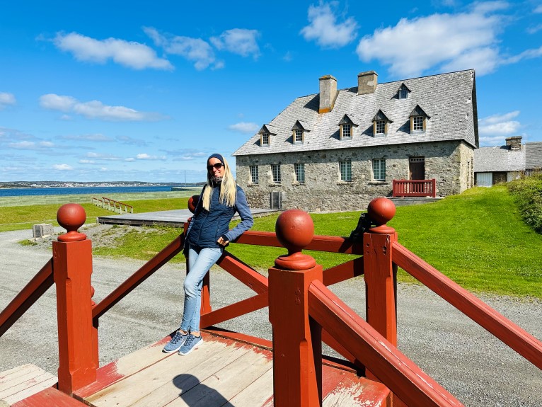 Festung von Louisbourg auf Cape Breton, Frau steht vor rotem Geländer vor einem Haus aus Stein