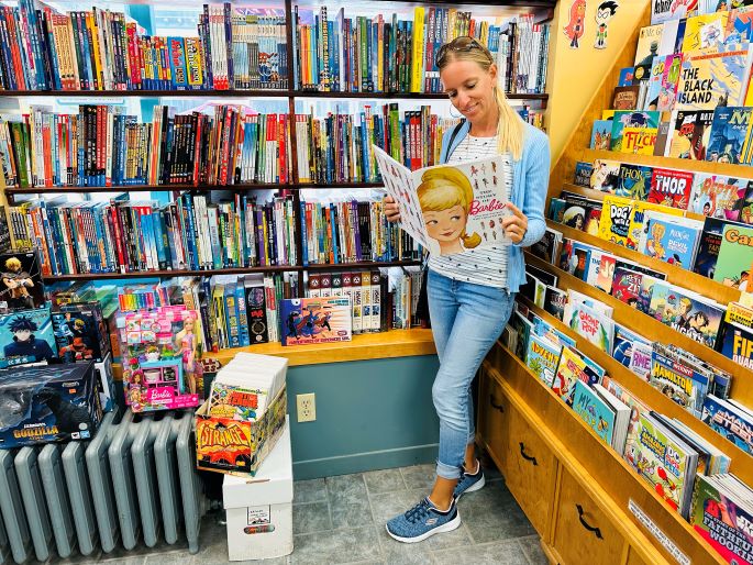 Halifax Sehenswürdigkeiten, Comic Shop Strange Adventures, Frau steht mit Barbie-Comic in der Hand vor Regalen mit Comic-Sammlungen