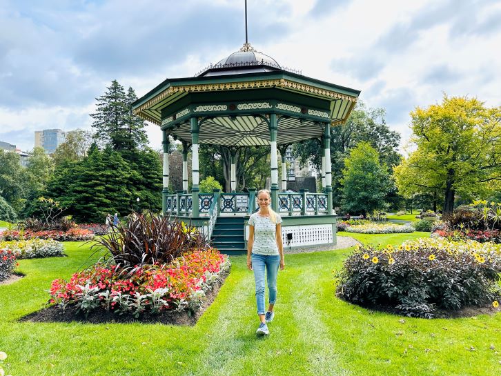 Halifax Sehenswürdigkeiten Public Gardens, Frau steht auf Rasen vor Pavilion mit bunten Blumen drumherum