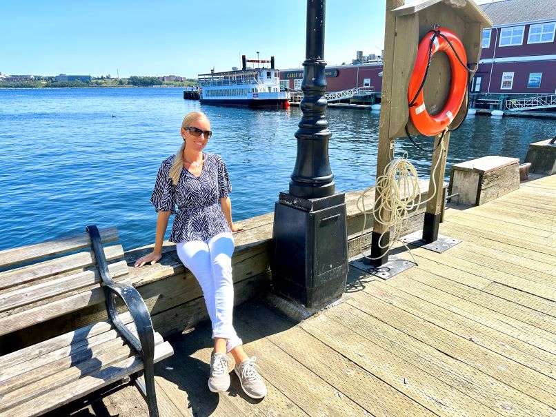 Halifax Sehenswürdigkeiten, Waterfront direkt am Wasser, Frau sitzt auf Holzbank, hinter ihr Wasser mit einem Boot