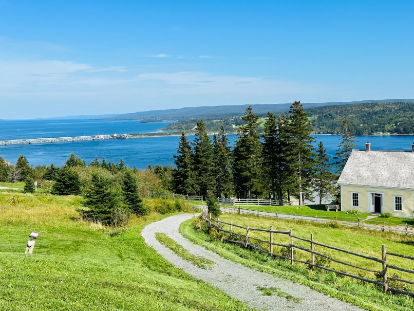 Highland Village Cape Breton. Nachgebaute Siedlung, Wiese, Haus und Blick auf See