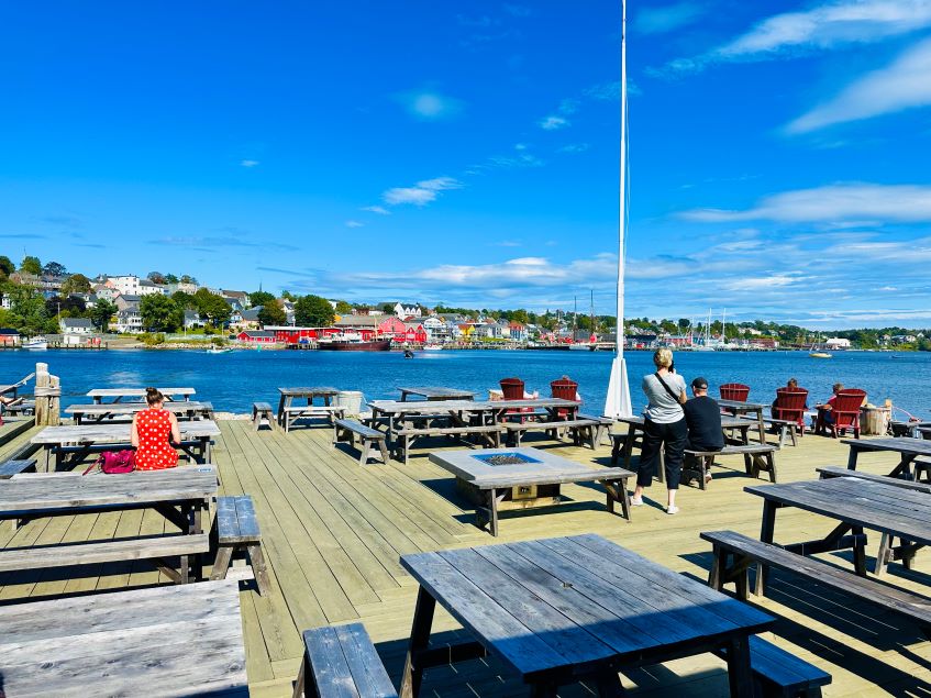 Tische und Stühle aus Holze bei der Lightship Brewery mit Blick auf das Wasser und den bunten Hafen von Lunenburg