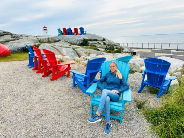 Peggys Cove, Frau sitzt auf buntem Holzstuhl mit Leuchtturm im Hintergrund