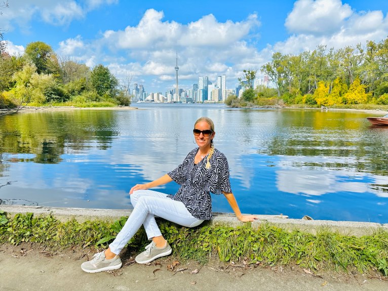 Frau sitzt auf Randstein vor Wasser mit Skyline von Toronto im Hintergrund