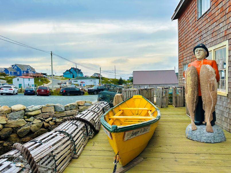 Gelbes Boot und Figur eines Mannes, der Fische in der Hand hält vor einem Souvenirshop in Peggys Cove